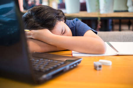 Child girl fall face down on the table, geet tired or feel sleepy during learning onlineの写真素材