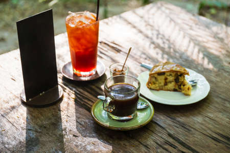 Black coffee with fruit cake and iced tea on table, morning sunlight with light meal in the garden