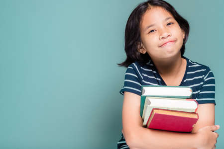 Ten years old girl sitting at green wall holding books in her arms