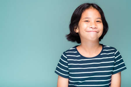 Head shot of Thai child in stripes T-shirt sitting at green wall and smile to the camera