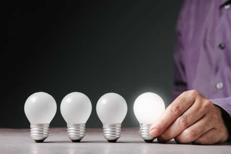 Closeup businessman choose the one of light bulb in a row that glowing brighter, best idea and select the right one, or different conceptの写真素材