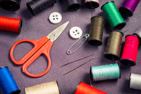 Small sewing tools kid for clothing amendment on gray cloth (small scissors and colorful thread spools with needle, pin and button)の写真素材