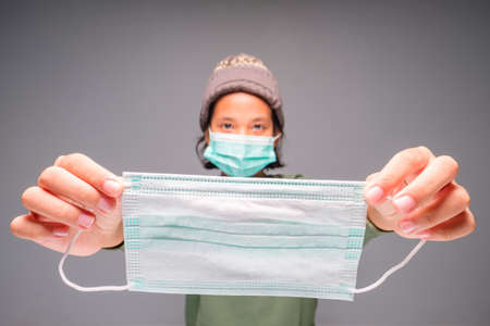 Child stretch out her hands with surgical mask from the back side to wear the mask to the others, prevention yourself from the virus conceptの写真素材