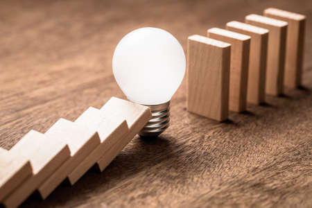 Glowing light bulb block the falling of domino in a rowの写真素材