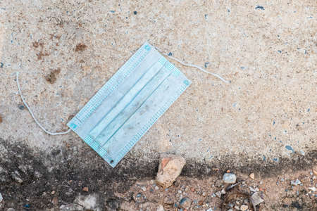 Closeup a dirty and torn surgical face mask become the garbage leaving on the ground along the street, covid-19 and environment, pandemic and endingの写真素材