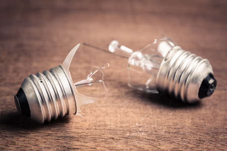 Two broken old light bulbs on wood table, problem and bad solution, time for change the light bulb or ideaの写真素材