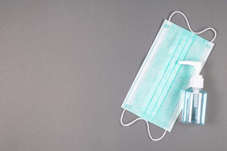Small alcohol spraying bottle and surgical face mask on gray paper