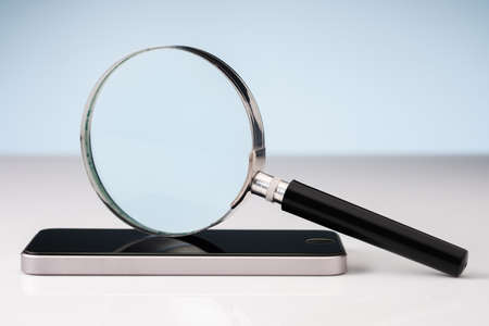 Closeup magnifying glass over the smartphone, searching and analyze information from social media, check up and detect mobile phone conceptの写真素材