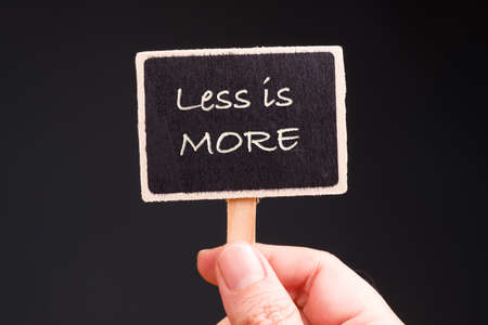 Closeup hand hold small notice sign made by wooden clothespin with text : Less is More,...