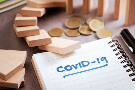 Covid-19 handwriting text on notebook with falling and coins on the desk, impact of covid-19...
