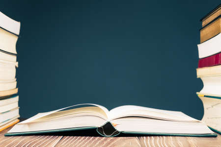 Opened book between pile of books on the table, blank wall as copy space