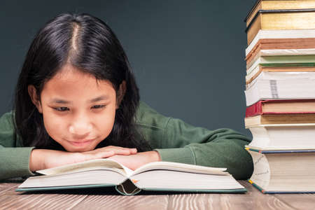 Ten years old girl intend to read the book on the table with a lot of books on pileの写真素材