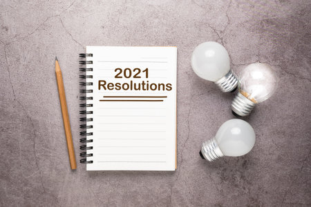 Opened small notebook with text : 2021 Resolutions, and glowing light bulbs as planning ideaの写真素材