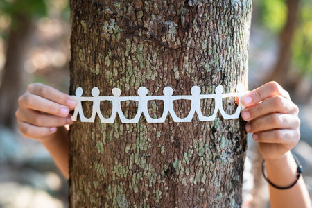 Closeup child hold the paper human chain around tree trunk in the forest, save and protect the tree,...