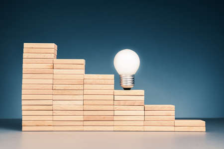 Glowing light bulb on stairstep wooden blocks, creativity moving step higher to successの写真素材