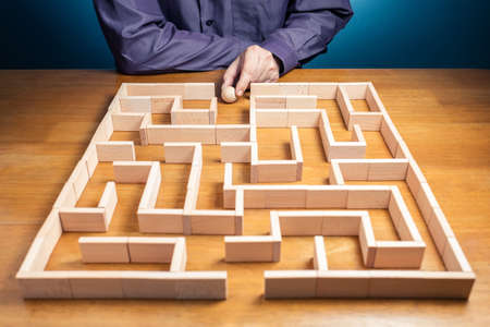 Man going to play the labyrinth game built by wood blocks on the table, find the right way to the exitの写真素材
