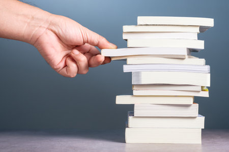 Closeup hand choosing the book from the pile of new pocket books on the tableの写真素材