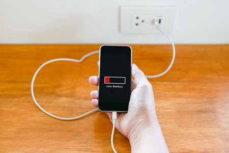 Hand hold the low battery phone while charging from the USB power socket on the wallの写真素材