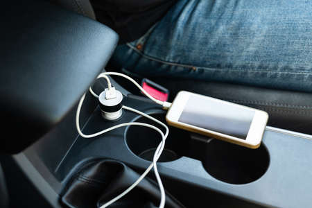 Closeup power socket and adapter charging phone battery on the center console in private care