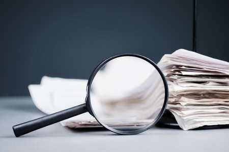 Magnifying glass with stack of receipts in paper nail on the desk, inspect income, sale analysis conceptの写真素材