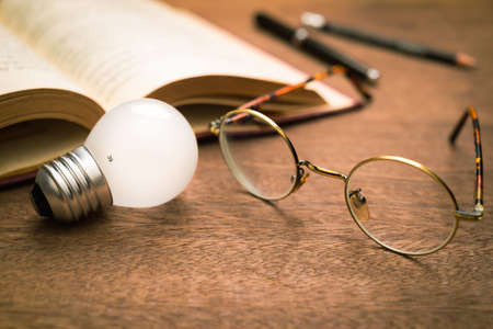 Closeup eyeglasses and light bulb with opened book and pencils on the table, intellectual reading for idea and inspirationの写真素材