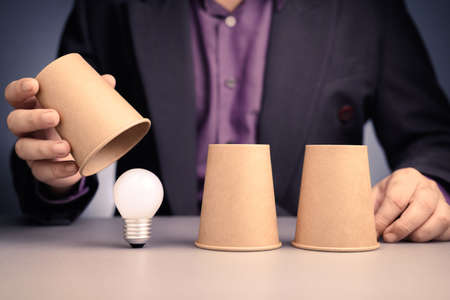 Man plays a three cups shell game and reveals the right one to find a light bulbの写真素材