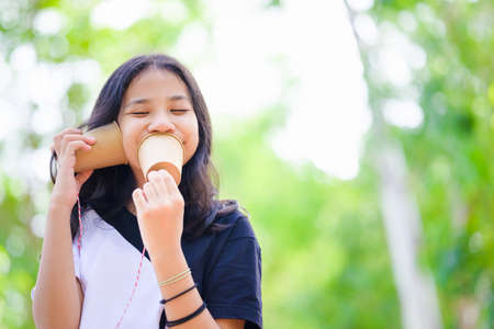 A joyful girl is fun to play with classic cup phone by talking and listening to herself in nature, mental health in childhoodの写真素材