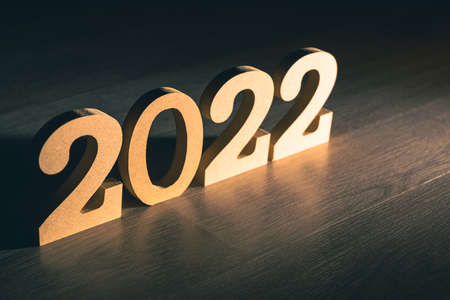 Wooden numbers of year:2022, stand on the table with light on dark background