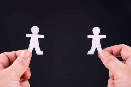 Hand hold the paper human separate from each other on black background, social distancing during coivd-19 pandemic, or making a connection conceptの写真素材