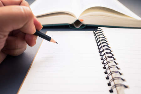 Closeup hand with pencil going to writing the content from the book, summarize the information, read...