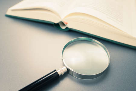 Magnifying glass and opened book on the desk, learning, research or searching information concept