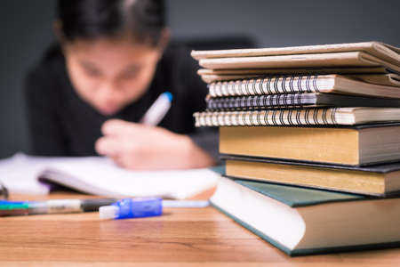 Closeup pile of textbooks and notebooks on the desk with child doing homework on background, much more homework to do during online education programの写真素材