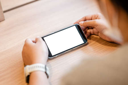 Closeup woman is watching the mobile phone on the table, with empty white screenの写真素材