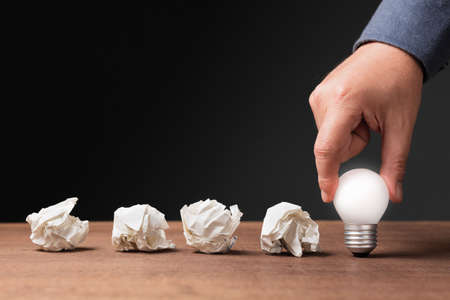 Hand put a glowing light bulb behind the row of crushed paper balls, the problems are the guideline to success, turn mistakes into power, motivation, and achievement conceptの写真素材