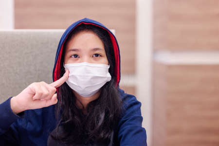 Eleven years old girl in hooded jacket is looking at the camera and reminded to wear the face mask in the restaurantの写真素材