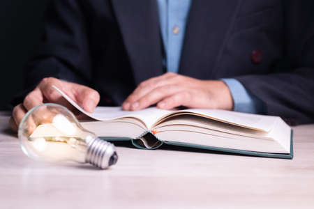 Businessman is reading the book with glowing light bulb on the desk, selective focus at the book, knowledge is powerの写真素材