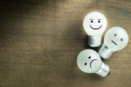 Satisfaction light bulb on wood background, excellent or happy smile face icon is glowing, with average and bad emotion as feedback and evaluation conceptの写真素材