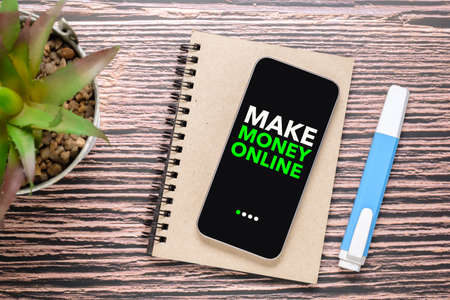 Make Money Online text on the screen of a small smart phone with a small notepad and a pen, concept of easy and convenient way to make money onlineの写真素材