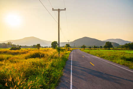 Asphalt road along the field to the mountain with sunset on the sky, travel scenic at Khao Luang Mountain near the Sukhothai Historical Park, Thailandの写真素材
