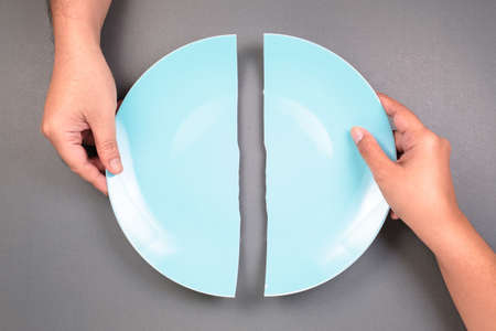 Hands of a man and a woman breaking the dish and split it as two halves, fracture problem in relationships that hard to conciliateの写真素材