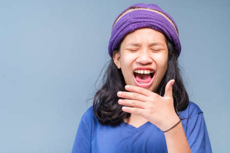 Child girl in blue t-shirt and knitting wool hat is laughing out loud (LOL), open mouth, and try to cover her mouth with handの写真素材