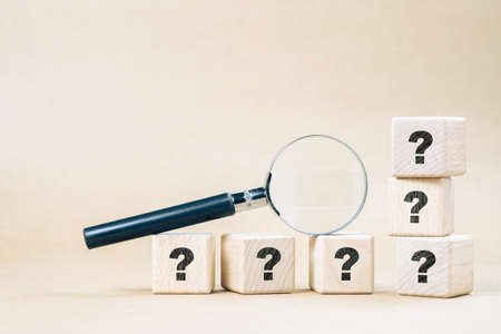 Magnifying glass on wood cubes with many question marks, confusing, frequently asked questions, and...