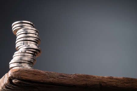 Unstable heap coins at the edge of the wood table with copy space, risk in financial conceptの写真素材