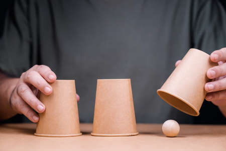 Closeup man playing a shell game, three cups with wooden ball, and reveal where the right position of the ball isの写真素材