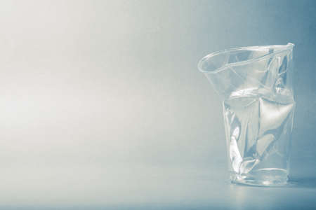 A crushed plastic cup, transparent drinking cup on faded background with copy spaceの写真素材