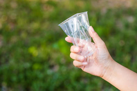 Closeup hand of a woman holding a crushed plastic cup in nature on green backgroundの写真素材