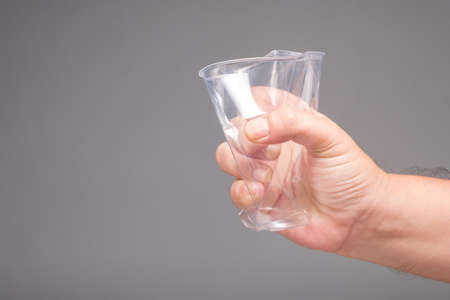 Closeup hand of a man crush a plastic cup on gray background in studio, get rid of plastic product conceptの写真素材