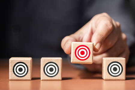 Closeup man pick one of wood blocks in a row with a different target symbol, choose or narrow your targetの写真素材