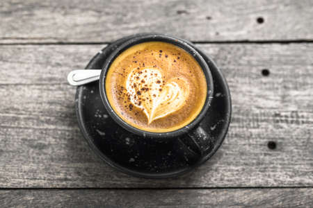 Cappuccino coffee in black ceramic cup on old wood plank table