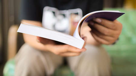 Closeup a woman is reading book in her hands while sitting on the sofa